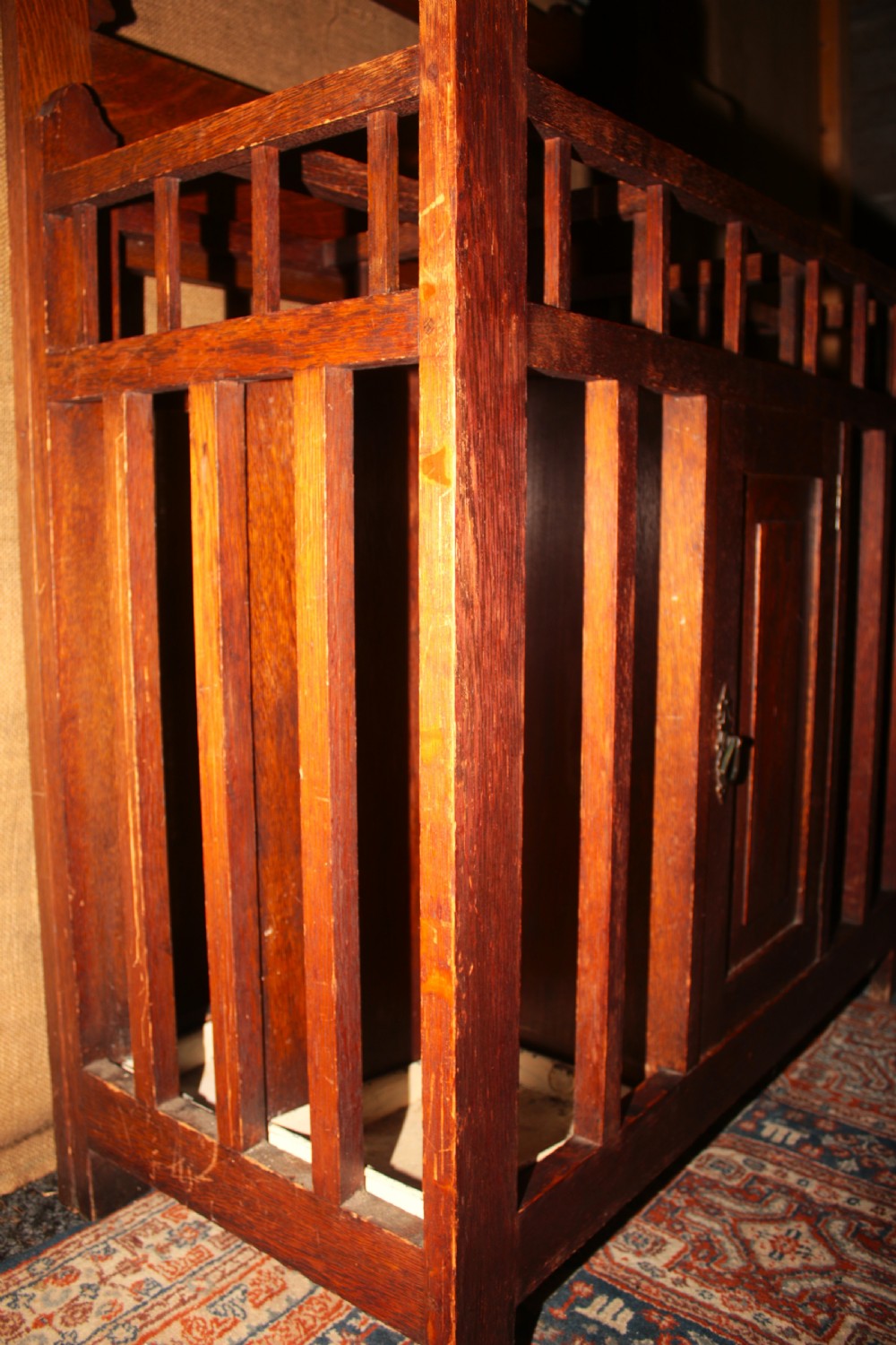 An Arts and Crafts oak hall stand featuring a central square mirror, metal coat hooks, umbrella drip trays, and a lower storage cupboard. View V