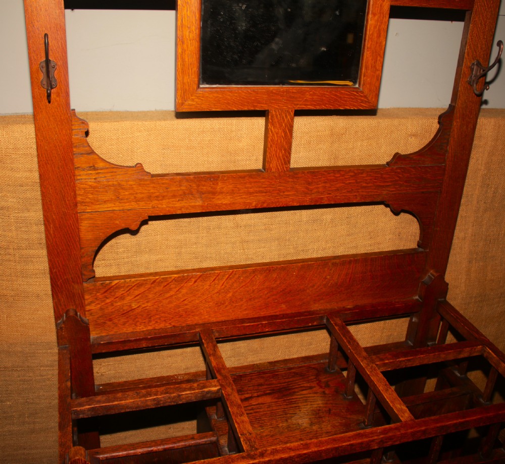 An Arts and Crafts oak hall stand featuring a central square mirror, metal coat hooks, umbrella drip trays, and a lower storage cupboard. View VI