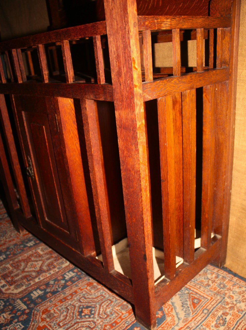An Arts and Crafts oak hall stand featuring a central square mirror, metal coat hooks, umbrella drip trays, and a lower storage cupboard. View VIII