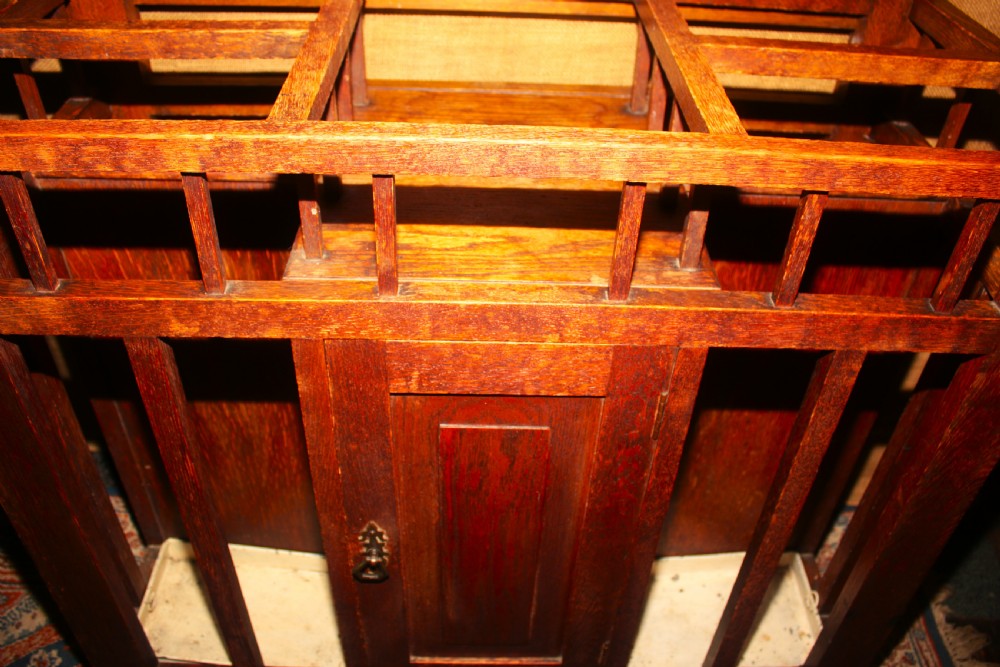 An Arts and Crafts oak hall stand featuring a central square mirror, metal coat hooks, umbrella drip trays, and a lower storage cupboard. View IX
