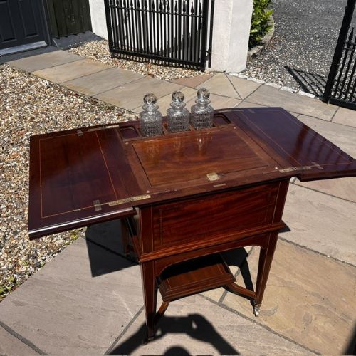 An Edwardian mahogany surprise drinks cabinet featuring satinwood inlay, square tapered legs, a lower shelf, and brass castors. View V