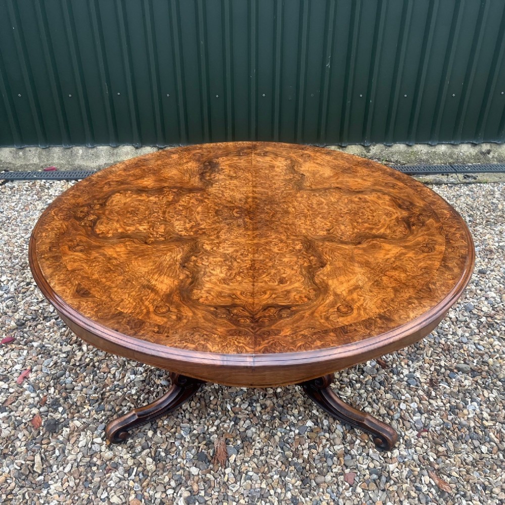 A circular Victorian dining table featuring a highly figured burr walnut top and a carved pedestal base.