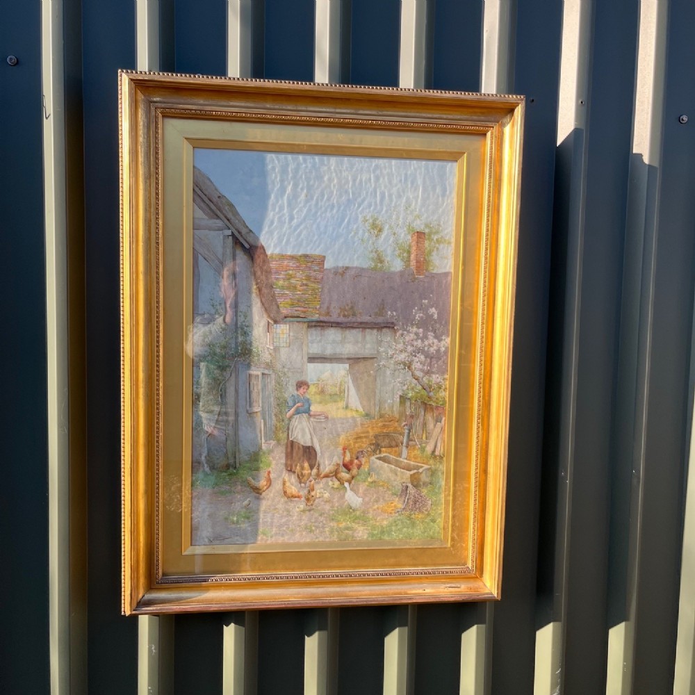 An Edwardian watercolour painting depicting a figure feeding chickens in a rural farmyard scene, presented in a gilded wooden frame.