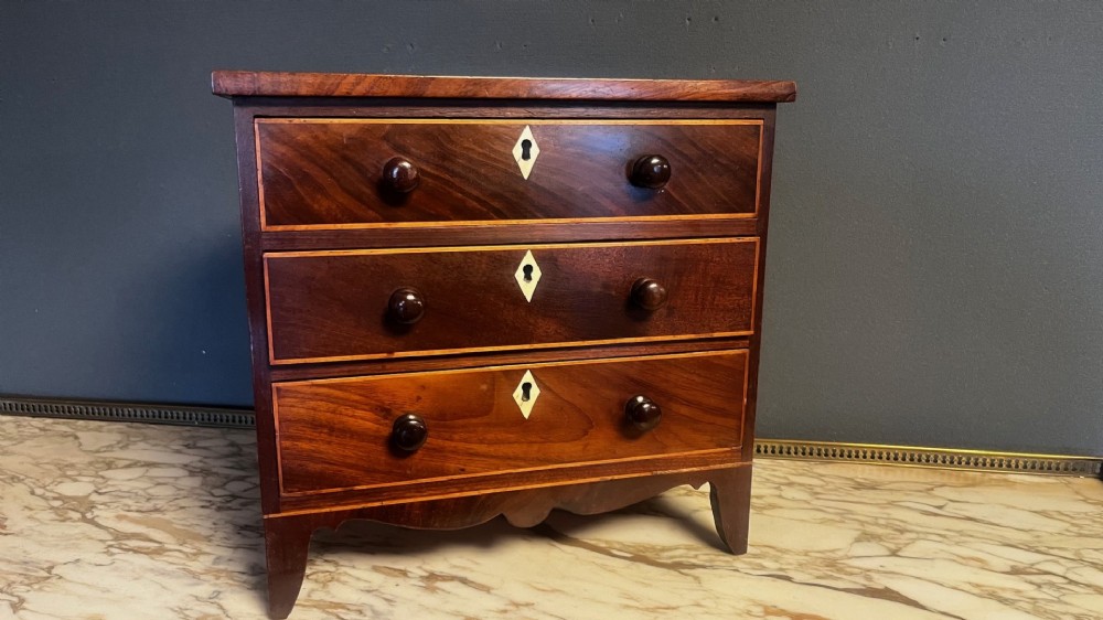 A small George IV period mahogany apprentice chest of drawers featuring three horizontal drawers with bone escutcheons and turned wooden knobs.