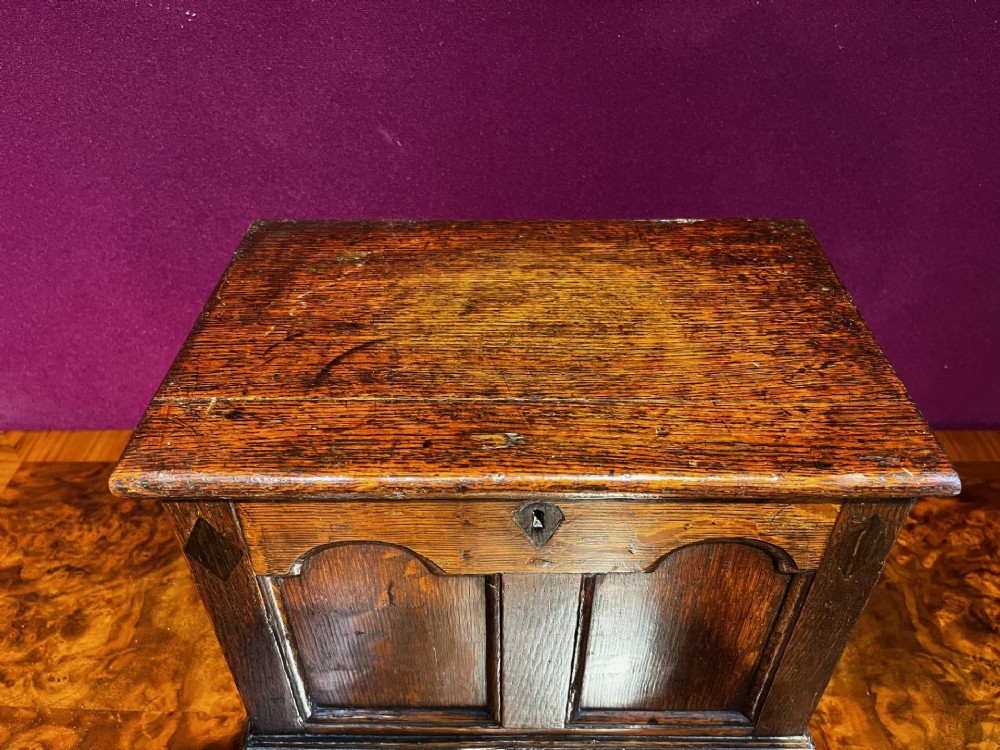 A late eighteenth-century miniature oak coffer with carved arched front panels, a kite-shaped inlay escutcheon, and a shaped apron base. View II
