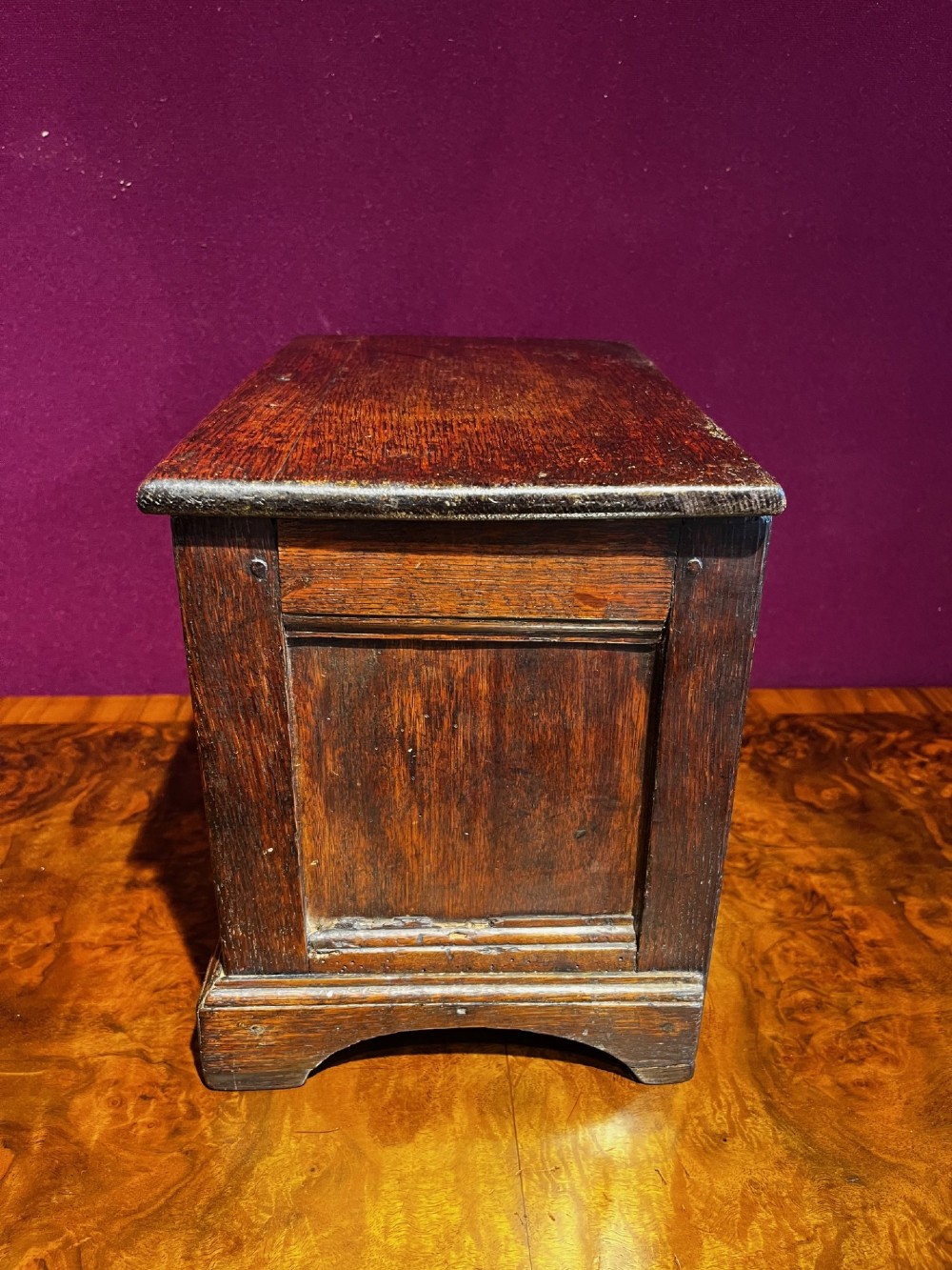 A late eighteenth-century miniature oak coffer with carved arched front panels, a kite-shaped inlay escutcheon, and a shaped apron base. View VI