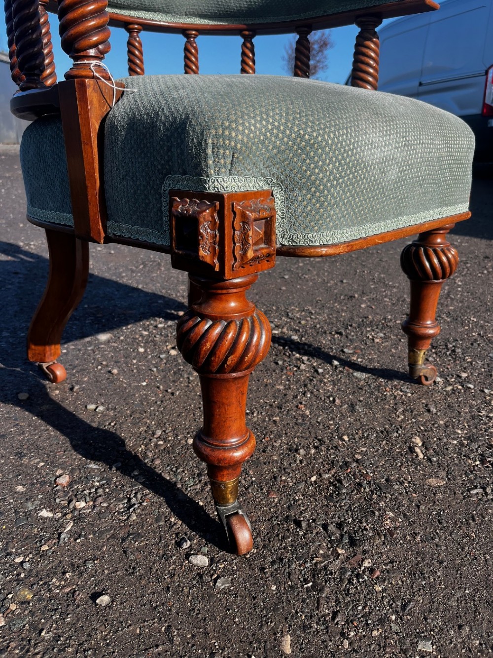 An antique Victorian walnut desk chair featuring a curved padded backrest, spiral-turned spindles, pale green textured upholstered seat, and turned legs on brass castors. View II