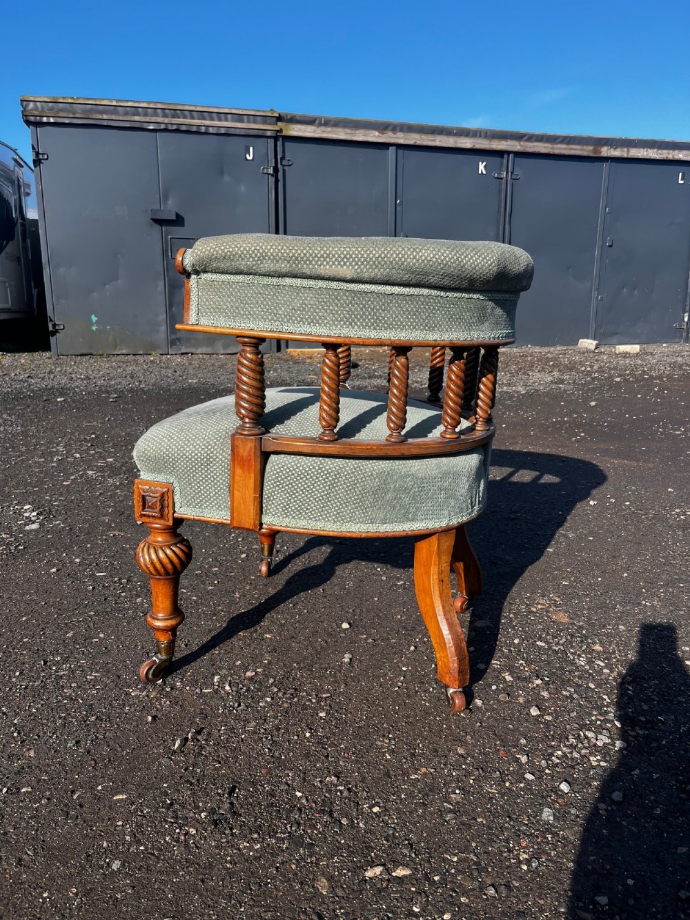 An antique Victorian walnut desk chair featuring a curved padded backrest, spiral-turned spindles, pale green textured upholstered seat, and turned legs on brass castors. View VII