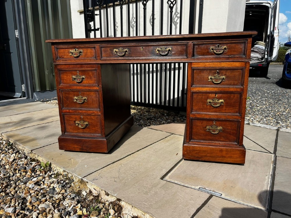 A late 19th-century mahogany pedestal desk featuring nine drawers with brass handles and a plinth base.