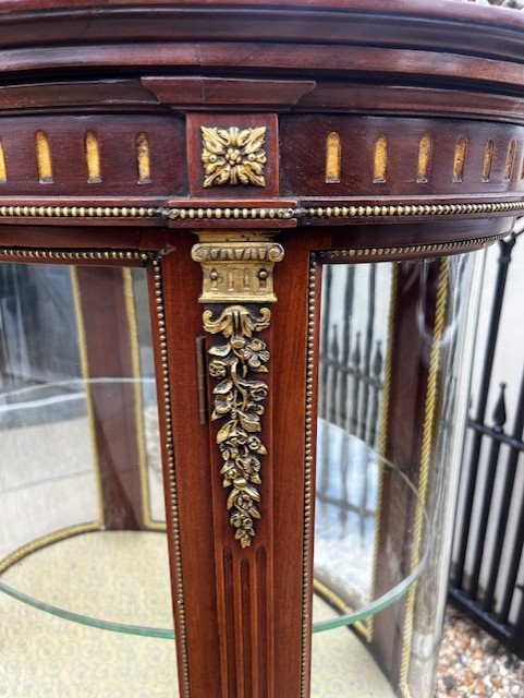An oval French mahogany vitrine featuring glass side panels, gilt-bronze ormolu mounts, fluted legs, and a gallery top above a lower undertier shelf. View II