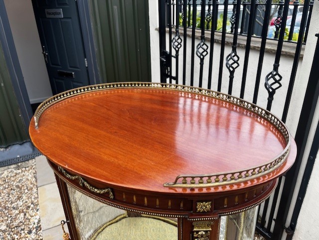An oval French mahogany vitrine featuring glass side panels, gilt-bronze ormolu mounts, fluted legs, and a gallery top above a lower undertier shelf. View III