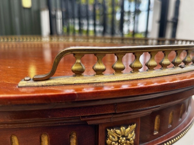 An oval French mahogany vitrine featuring glass side panels, gilt-bronze ormolu mounts, fluted legs, and a gallery top above a lower undertier shelf. View IV