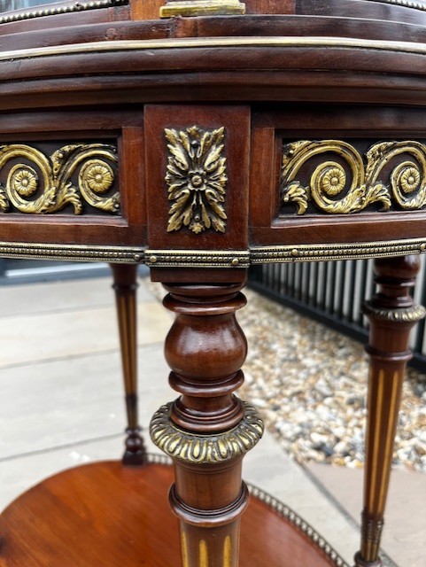 An oval French mahogany vitrine featuring glass side panels, gilt-bronze ormolu mounts, fluted legs, and a gallery top above a lower undertier shelf. View VI