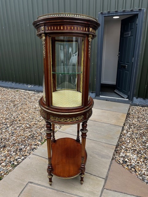 An oval French mahogany vitrine featuring glass side panels, gilt-bronze ormolu mounts, fluted legs, and a gallery top above a lower undertier shelf. View VIII