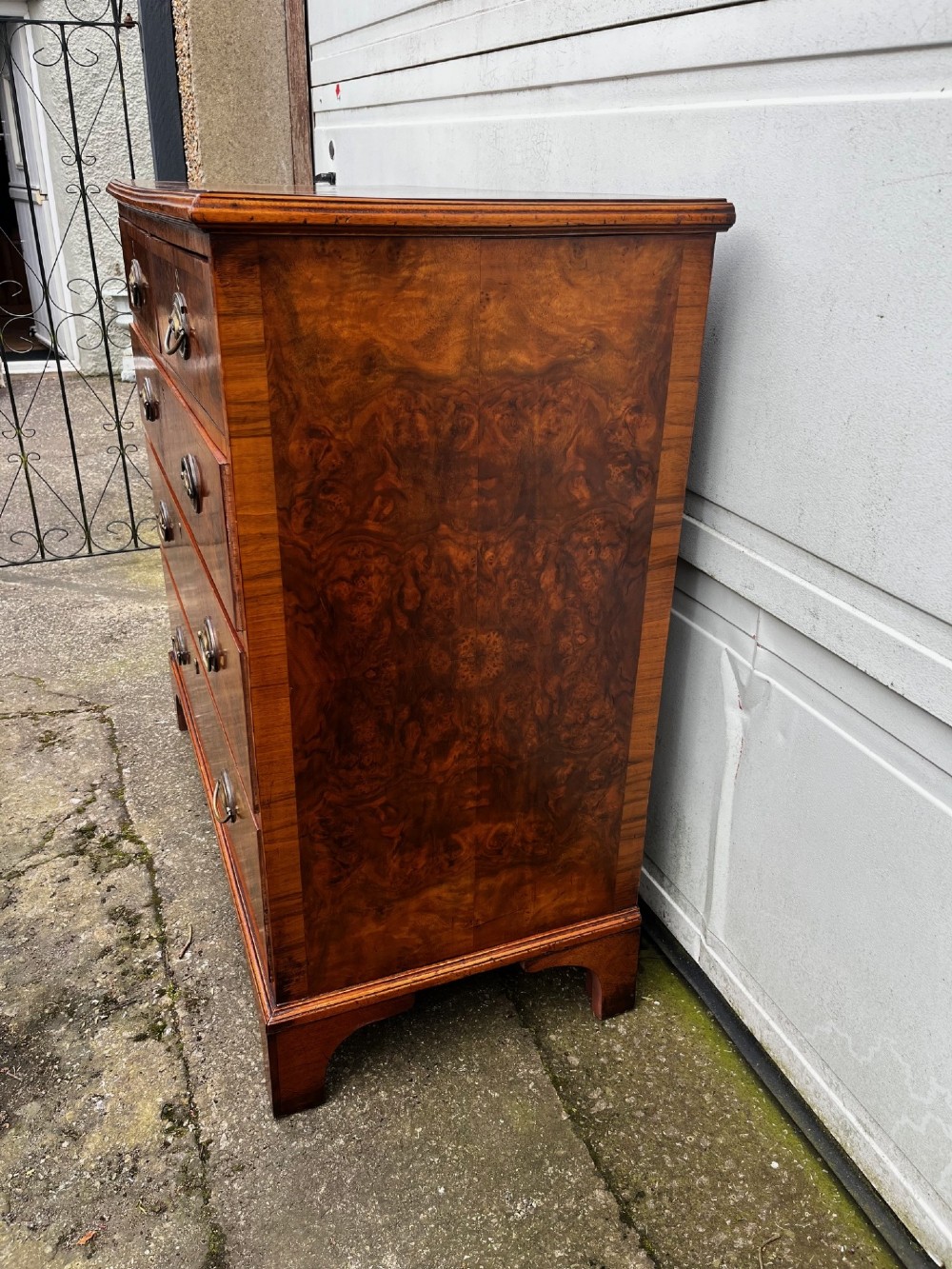 A 19th-century burr walnut veneered chest of drawers featuring two short over three long drawers with brass drop handles and bracket feet. View VI