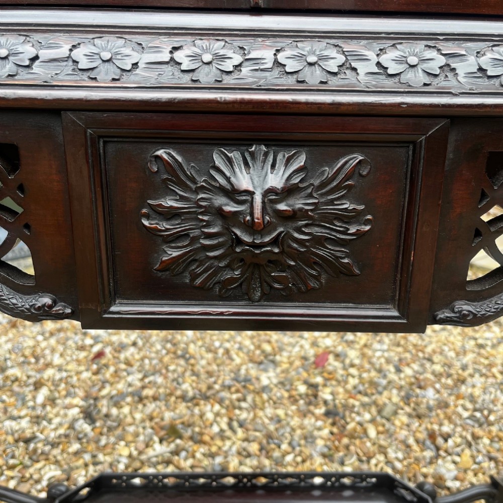 A tall dark mahogany Chinese Chippendale style display cabinet featuring glazed doors with gothic tracery, intricate pierced fretwork gallery, and a decorative carved stand with lattice legs. View II