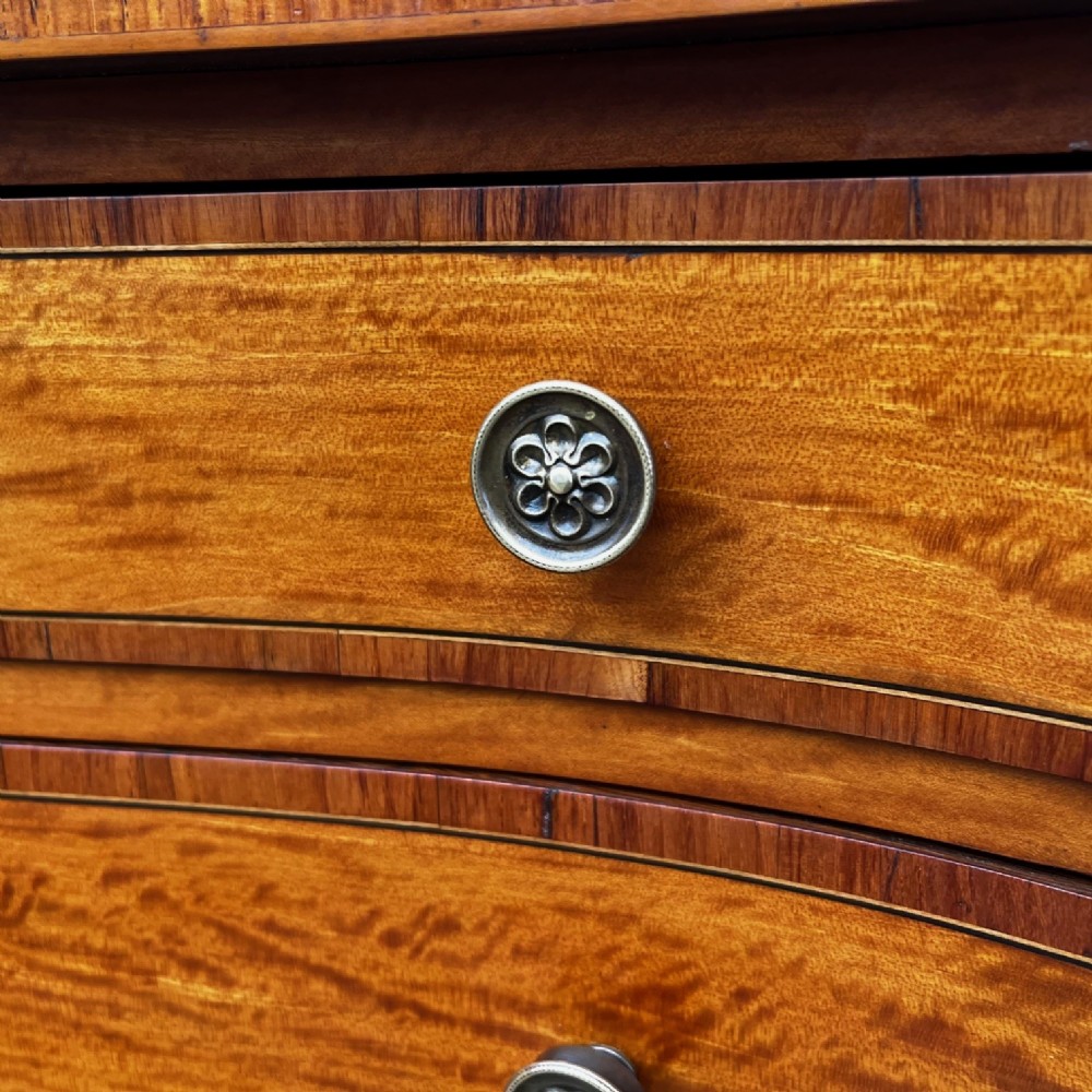 An antique Sheraton Revival satinwood display cabinet featuring arched astragal glazed doors, two lower drawers with ring handles, and square tapered legs. View III