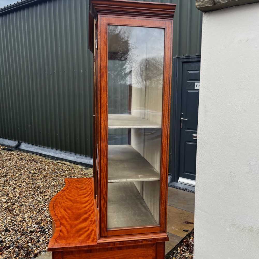An antique Sheraton Revival satinwood display cabinet featuring arched astragal glazed doors, two lower drawers with ring handles, and square tapered legs. View IX