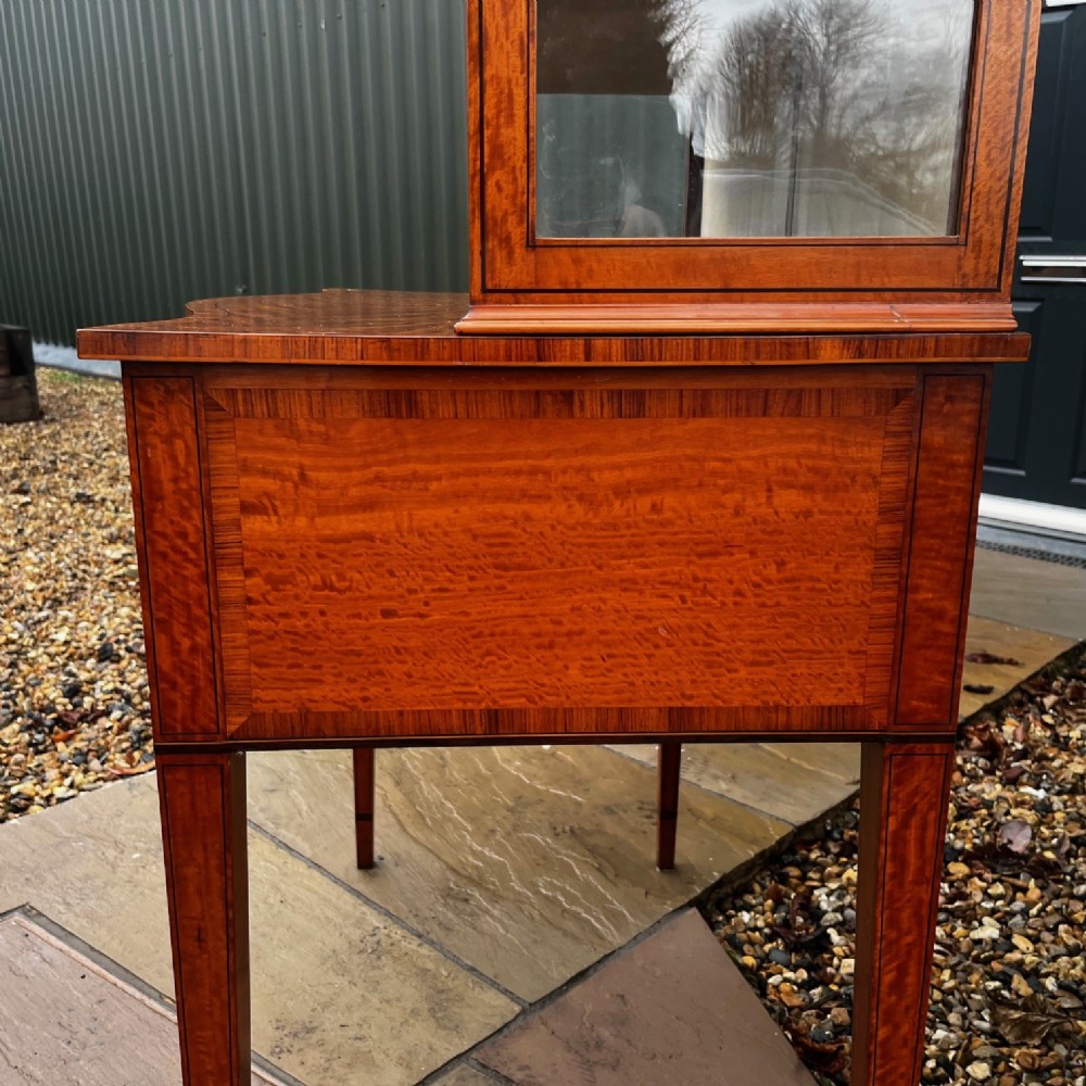 An antique Sheraton Revival satinwood display cabinet featuring arched astragal glazed doors, two lower drawers with ring handles, and square tapered legs. View X