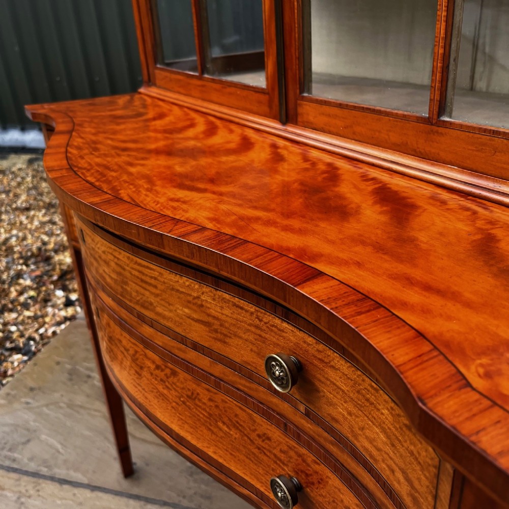 An antique Sheraton Revival satinwood display cabinet featuring arched astragal glazed doors, two lower drawers with ring handles, and square tapered legs. View XI