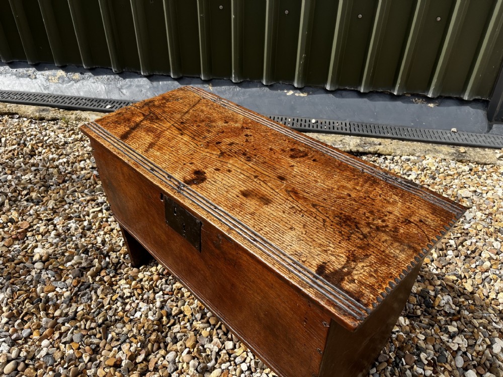 A solid dark oak 17th-century plank coffer featuring simple moulded border detailing, slab sides forming legs, and an iron lock plate. View II