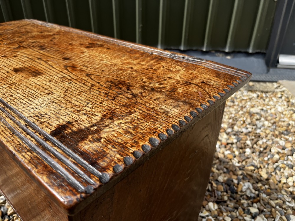 A solid dark oak 17th-century plank coffer featuring simple moulded border detailing, slab sides forming legs, and an iron lock plate. View III