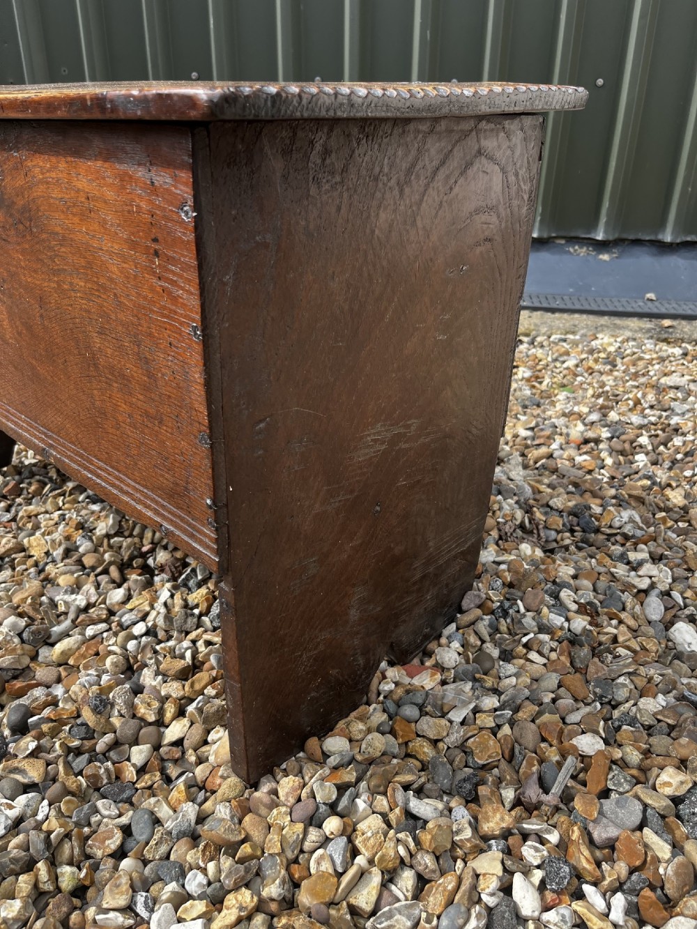 A solid dark oak 17th-century plank coffer featuring simple moulded border detailing, slab sides forming legs, and an iron lock plate. View V
