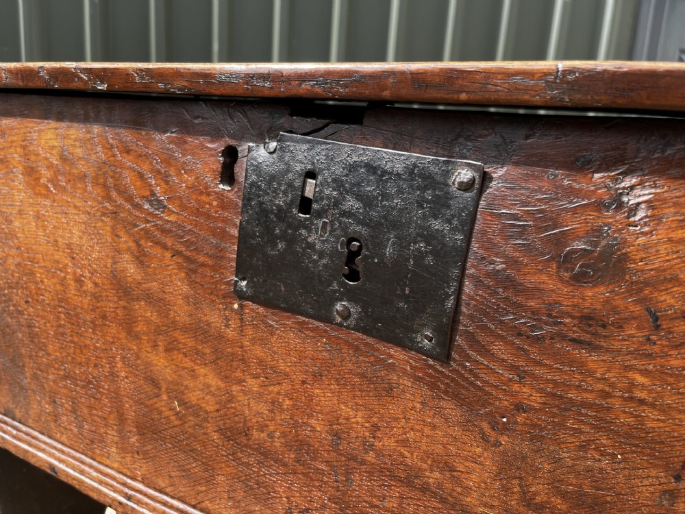 A solid dark oak 17th-century plank coffer featuring simple moulded border detailing, slab sides forming legs, and an iron lock plate. View VI
