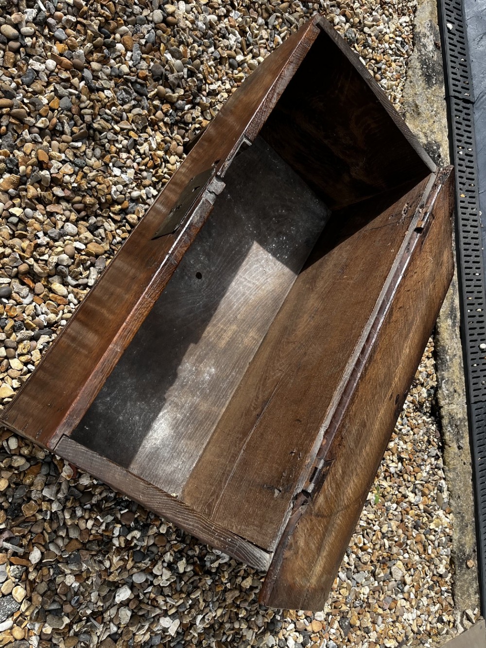 A solid dark oak 17th-century plank coffer featuring simple moulded border detailing, slab sides forming legs, and an iron lock plate. View VII