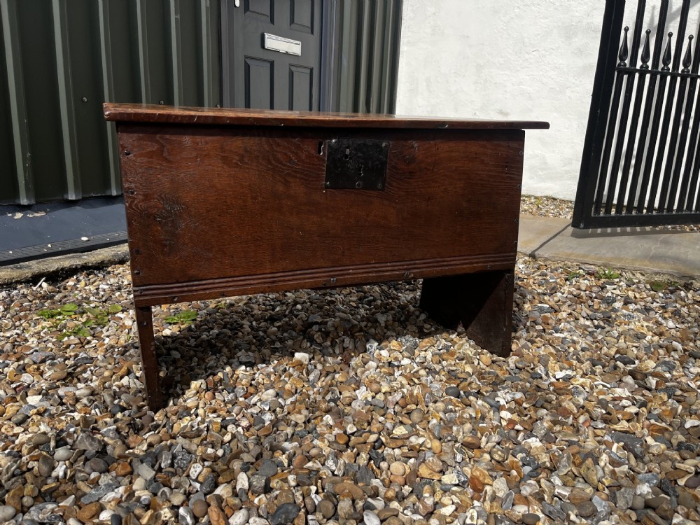 A solid dark oak 17th-century plank coffer featuring simple moulded border detailing, slab sides forming legs, and an iron lock plate. View IX