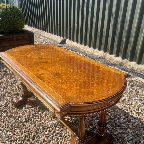 A Victorian burr walnut library table with shaped ends, fluted dual end supports, a low stretcher, and gilded ormolu mounts. View IV