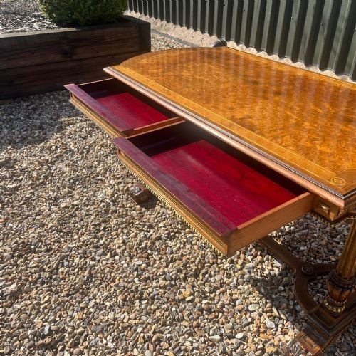 A Victorian burr walnut library table with shaped ends, fluted dual end supports, a low stretcher, and gilded ormolu mounts. View IX