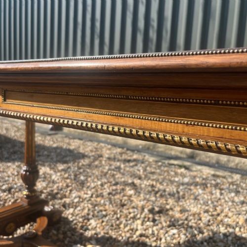 A Victorian burr walnut library table with shaped ends, fluted dual end supports, a low stretcher, and gilded ormolu mounts. View X