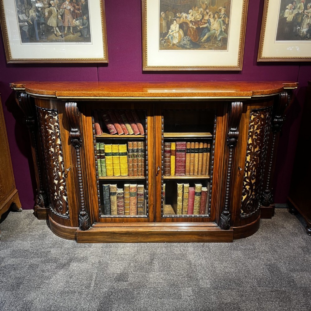 An early Victorian Goncalo Alves and amboyna low bookcase credenza featuring glazed doors and carved corbels.