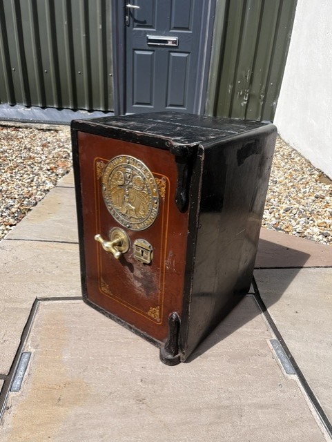 A Victorian cast iron safe featuring a black outer body, maroon door with gold pinstriping, and a round brass Cyrus Price & Co maker badge.