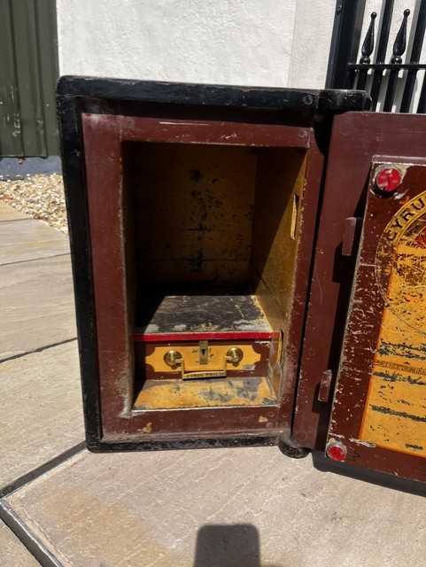 A Victorian cast iron safe featuring a black outer body, maroon door with gold pinstriping, and a round brass Cyrus Price & Co maker badge. View V