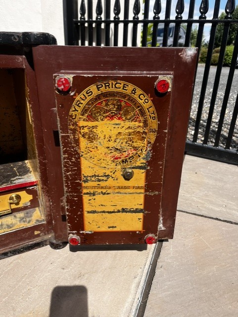 A Victorian cast iron safe featuring a black outer body, maroon door with gold pinstriping, and a round brass Cyrus Price & Co maker badge. View VI