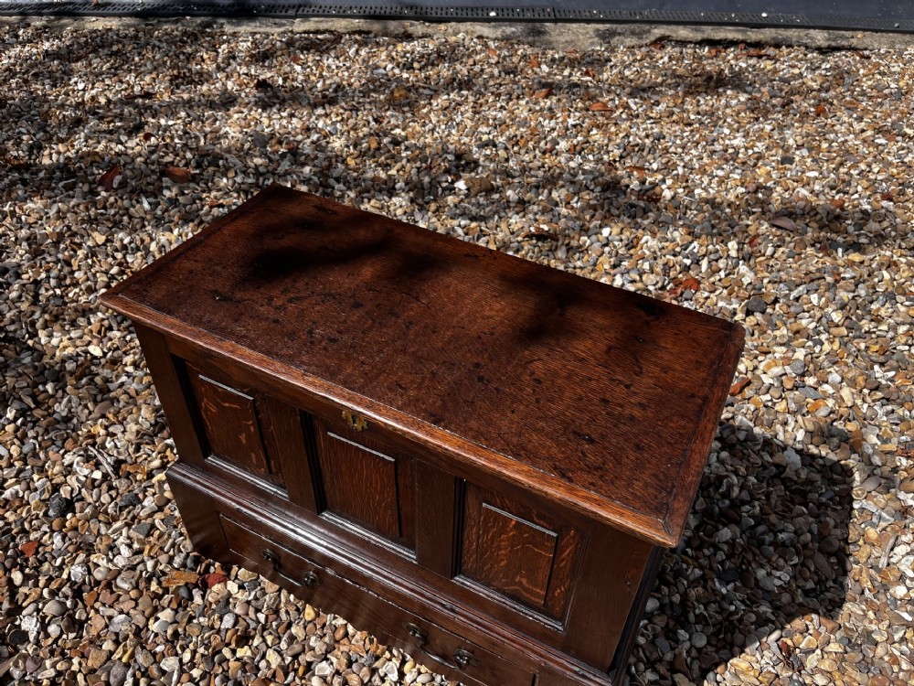 An eighteenth-century dark oak Welsh coffer bach featuring three fielded front panels, a lower drawer with brass handles, and a hinged lid. View V