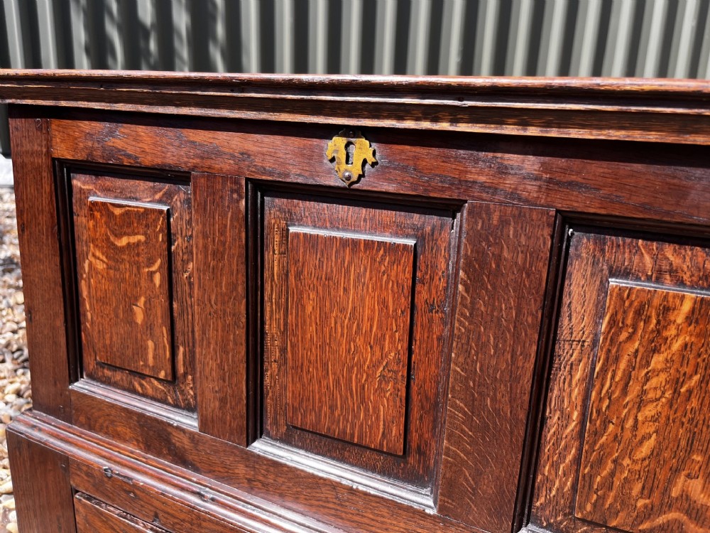 An eighteenth-century dark oak Welsh coffer bach featuring three fielded front panels, a lower drawer with brass handles, and a hinged lid. View VII