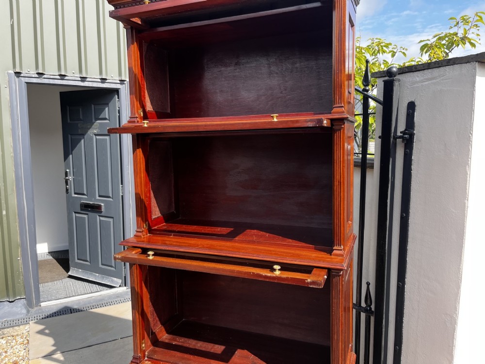 A four-tier solid mahogany barrister stacking bookcase featuring glazed up-and-over doors with brass knobs and a moulded top cornice. View VI