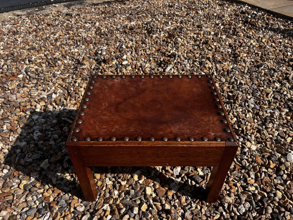 A rectangular Arts and Crafts oak stool featuring a brown leather top secured with a row of decorative metal studs around the rim. View II