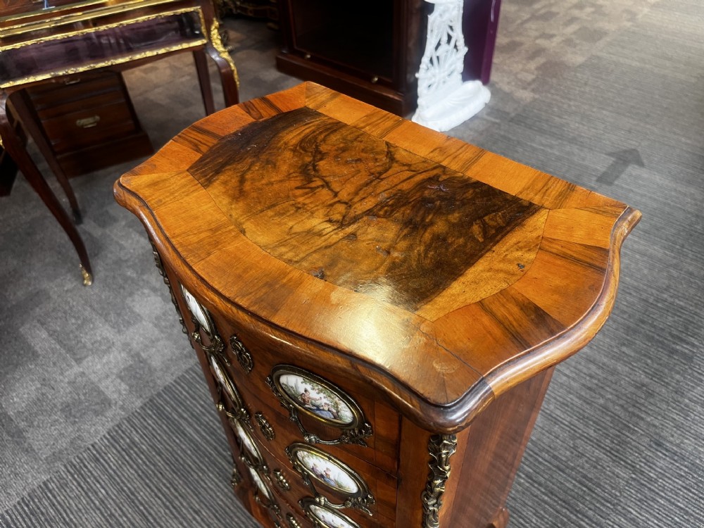 A late nineteenth-century walnut serpentine chest of four drawers featuring hand-painted oval porcelain plaques, ornate metal mounts, and slender cabriole legs. View II