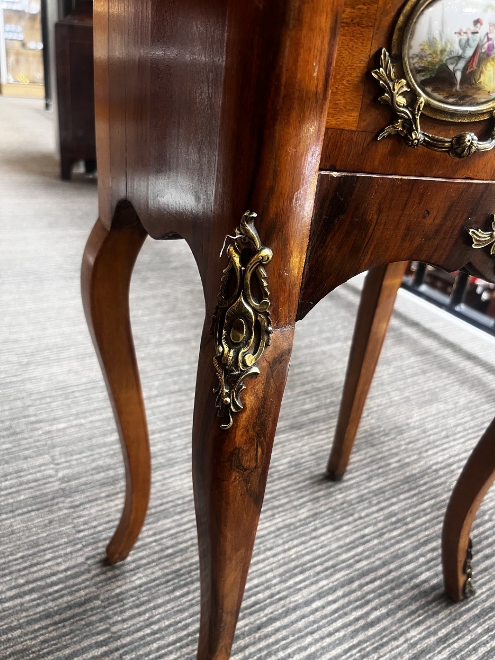 A late nineteenth-century walnut serpentine chest of four drawers featuring hand-painted oval porcelain plaques, ornate metal mounts, and slender cabriole legs. View V
