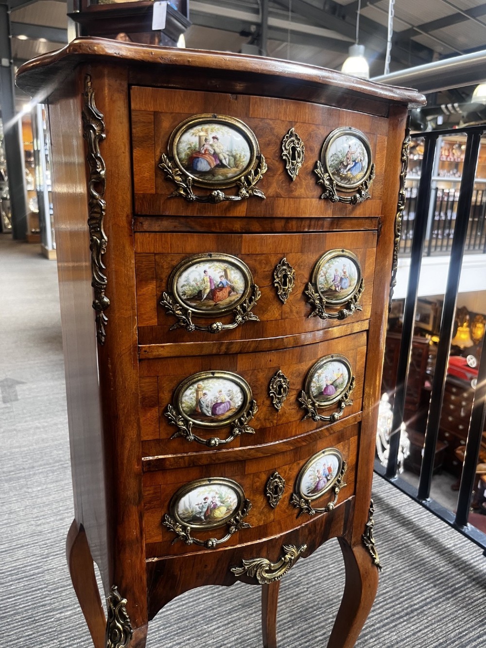 A late nineteenth-century walnut serpentine chest of four drawers featuring hand-painted oval porcelain plaques, ornate metal mounts, and slender cabriole legs. View VI