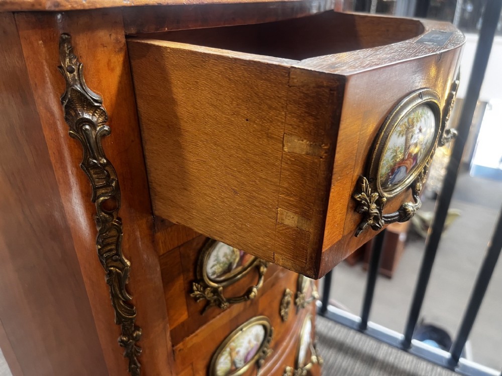 A late nineteenth-century walnut serpentine chest of four drawers featuring hand-painted oval porcelain plaques, ornate metal mounts, and slender cabriole legs. View X