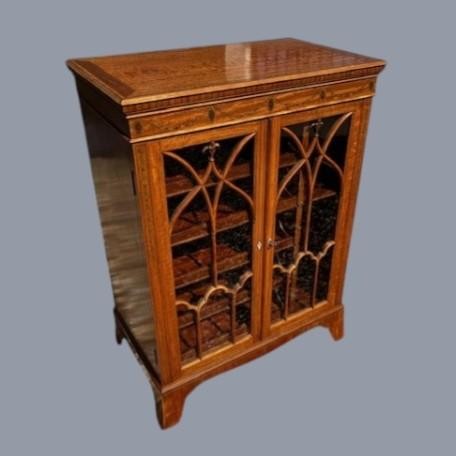 A late Victorian satinwood collectors cabinet featuring marquetry inlay details, Gothic style glazed double doors, and interior drawers.