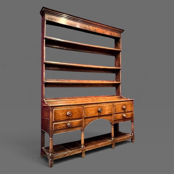 An early 19th-century dark oak Welsh dresser featuring a tall three-shelf open plate rack mounted on a base with five drawers, turned legs, and a lower pot board shelf. View III