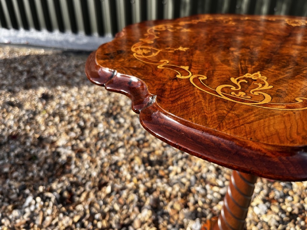 A Victorian burr walnut wine table featuring a scalloped top with floral marquetry inlay, a carved central pedestal, and tripod legs. View V