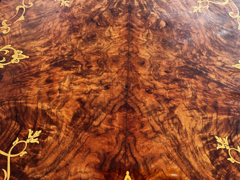 A Victorian burr walnut wine table featuring a scalloped top with floral marquetry inlay, a carved central pedestal, and tripod legs. View VI