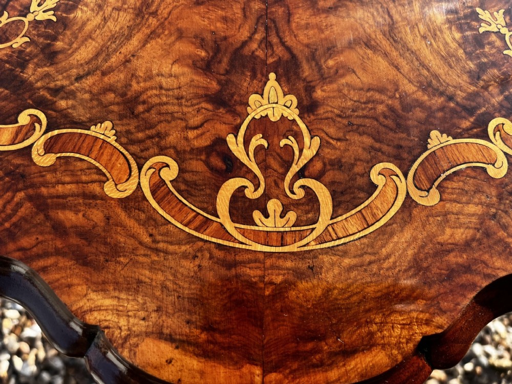 A Victorian burr walnut wine table featuring a scalloped top with floral marquetry inlay, a carved central pedestal, and tripod legs. View VII
